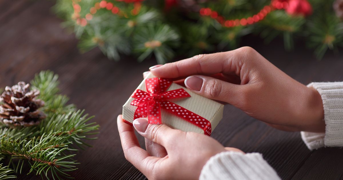 Két kéz egy apró ajándékot ad át, az ajándékozás szeretetteljes gesztusát jelképezve.