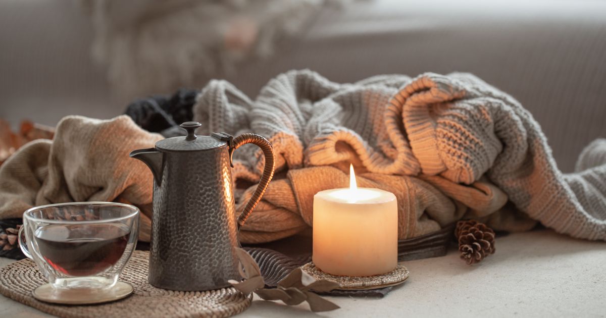 Gyertya, teásbögre és takaró egy nyugodt, öngondoskodó téli pillanatban.
